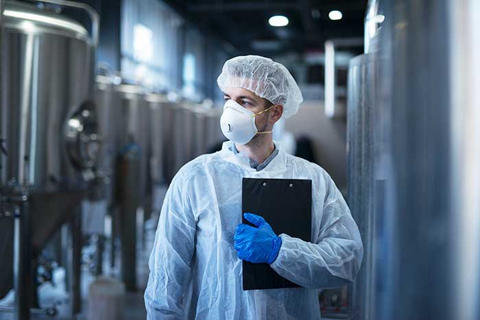 Technologist in protective white suit with hairnet and mask