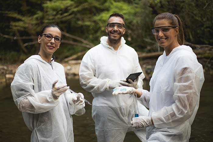 Scientist in protective suits taking water samples from the river