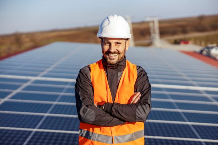 Smiling solar panel installer standing on top of a roof